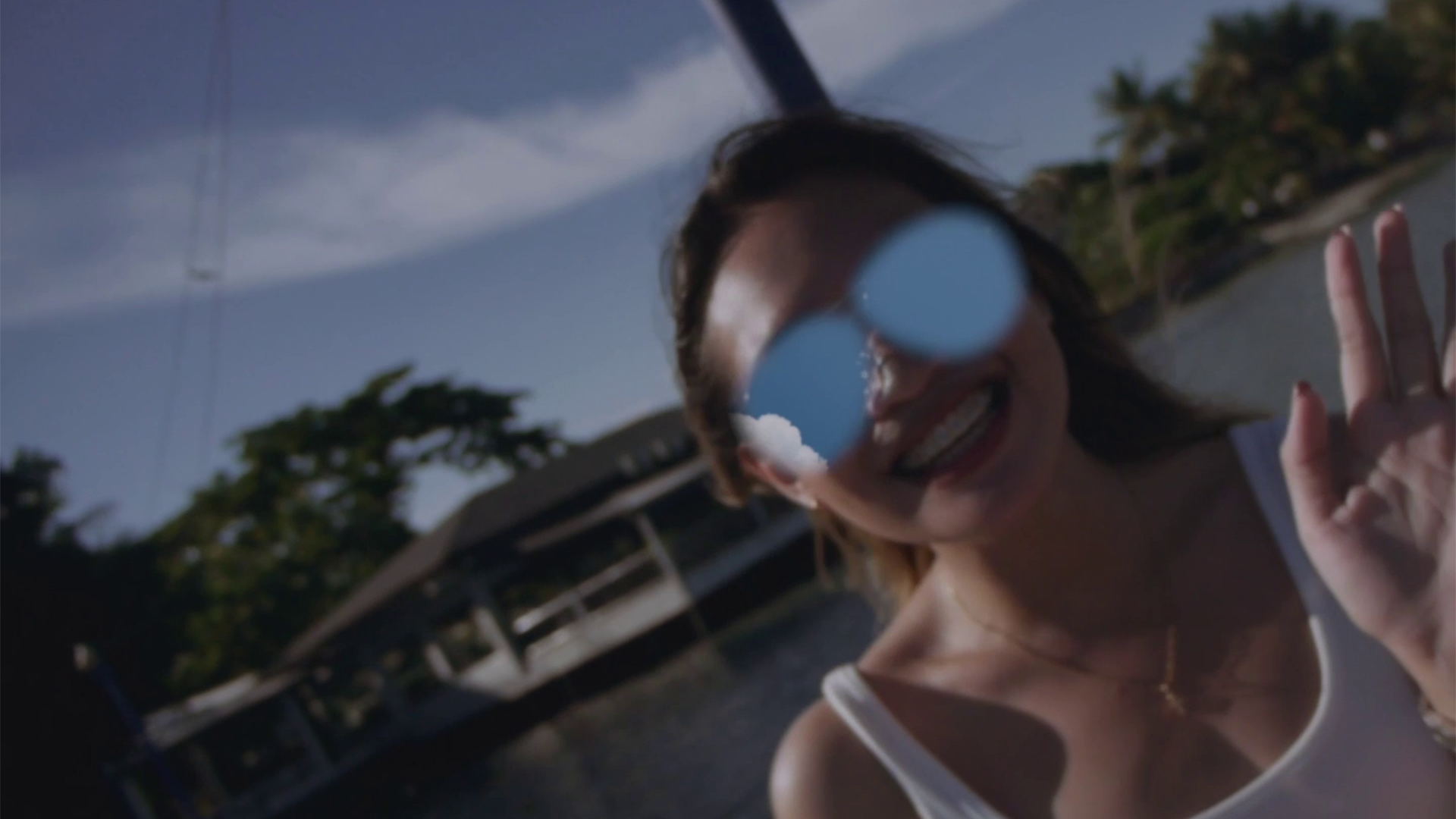 Megan smiling and waving at you, her shades reflecting blue sky in eerie way